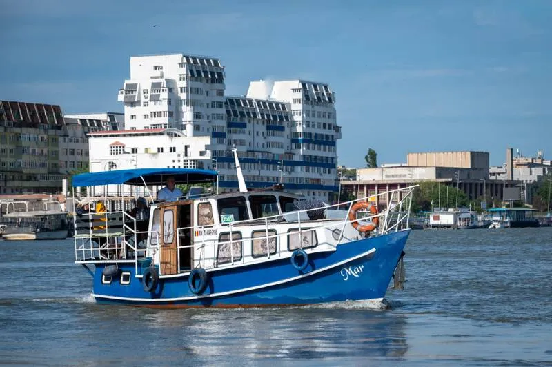 Barcă pe apă lângă clădiri urbane, cer senin.
