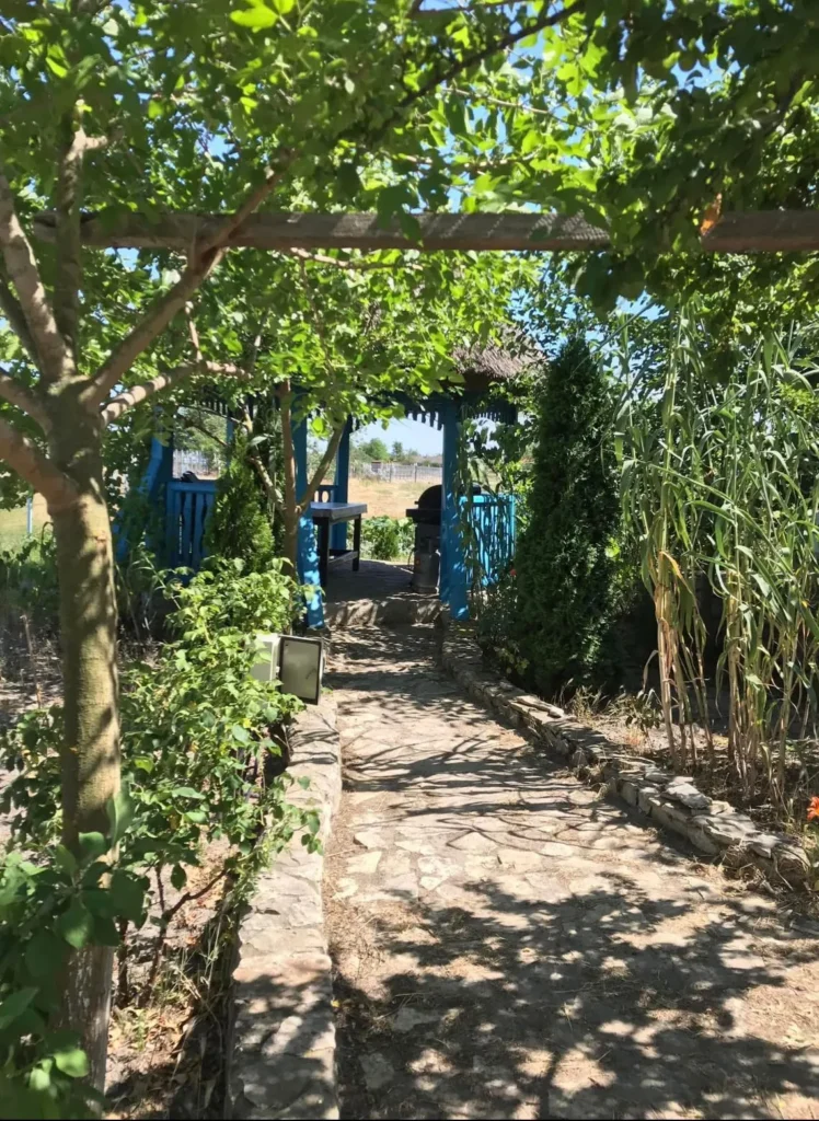 Aleee pietruită spre foișor albastru în grădină verde.